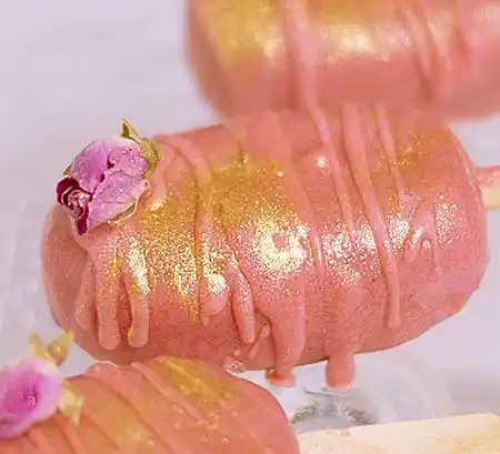 Rosafarbene Cakesicles mit Goldpulver und Miniröschen.