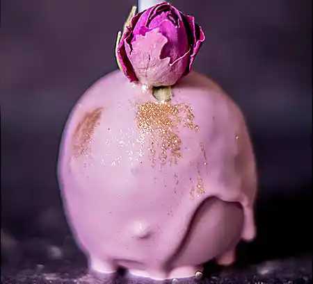 Rosafarbener Cake-Pop mit Goldpulver und Mini-Röschen als Deko..