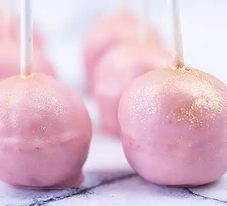 Rosafarbene Cake-Pops mit Goldsprenkel auf Marmorplatte.