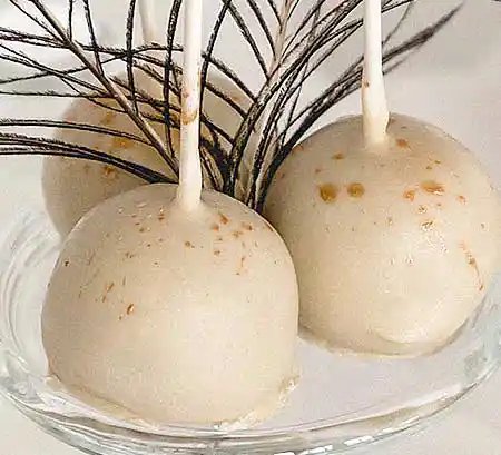 Weiße Cake-Pops mit Goldsprenkeln und Pfauenfeder als Deko.