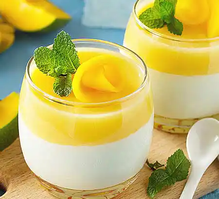Gläser mit Mango-Panna-Cotta aus gekochter Sahne mit Mango-Gelee, mit Garnitur aus Minze und Mango-Rose.