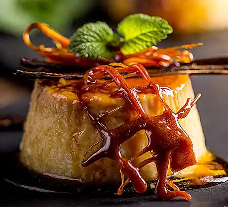 Teller mit Crème Caramel aus Sahne mit frischer Bourbon-Vanille, Karamelnetz und Minzgarnitur.