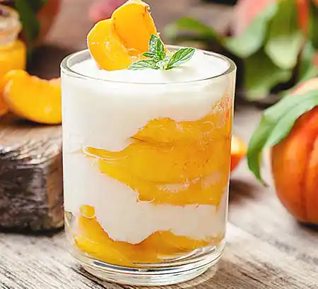 Glas mit Mascarpone-Creme mit friscchem Pfirsichragout und Minzgarnitur.