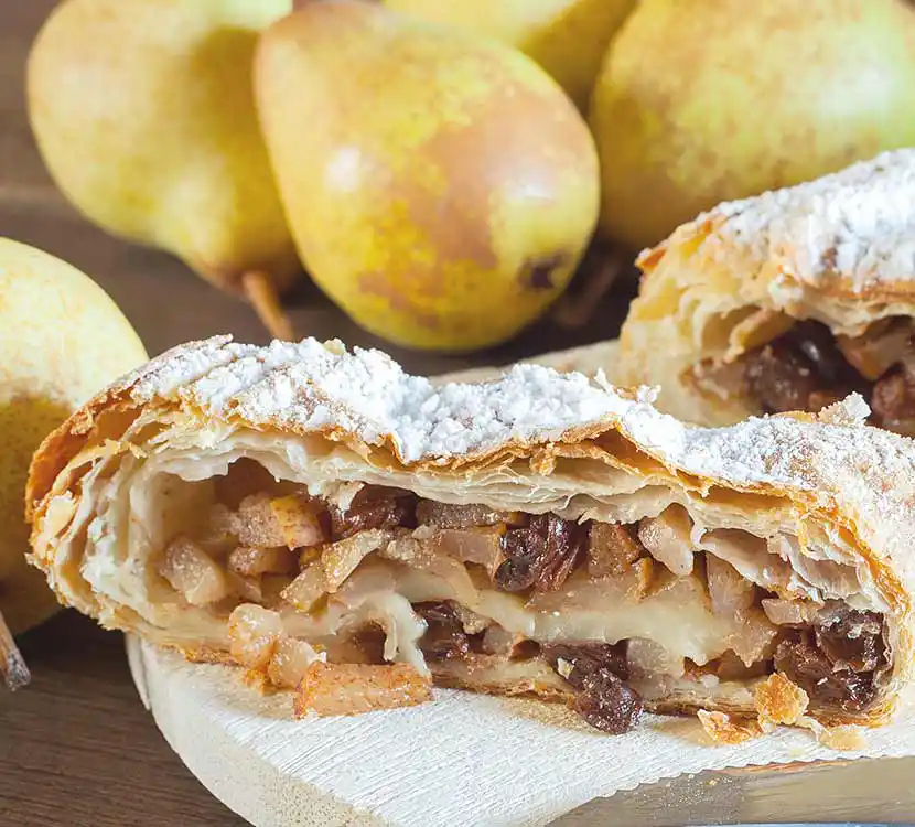 Angeschnittener Birnenstrudel auf Holtisch mit ganzen Birnen.