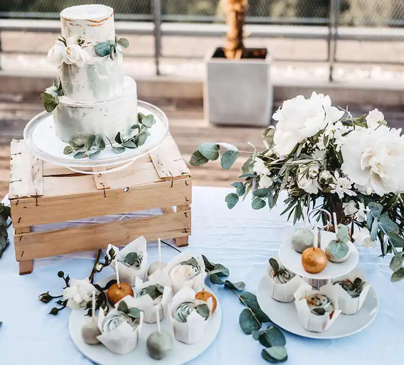 Gedeckter Tisch mit Hochzeitstorte auf Holzkiste, Cupcakes und Cakepops auf Teller.