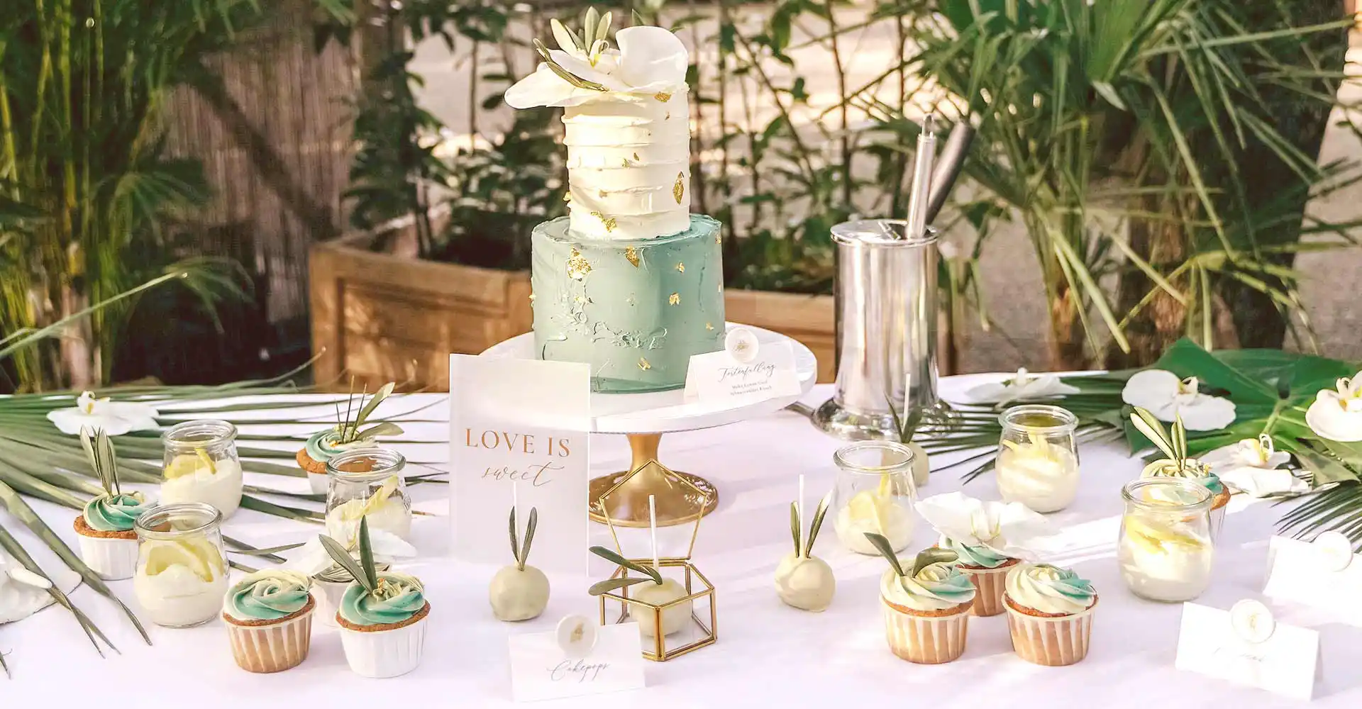Gedeckter Tisch mit Hochzeitstorte, Cupcakes und Cakepops auf Tellern angerichtet mit Blumendekor.