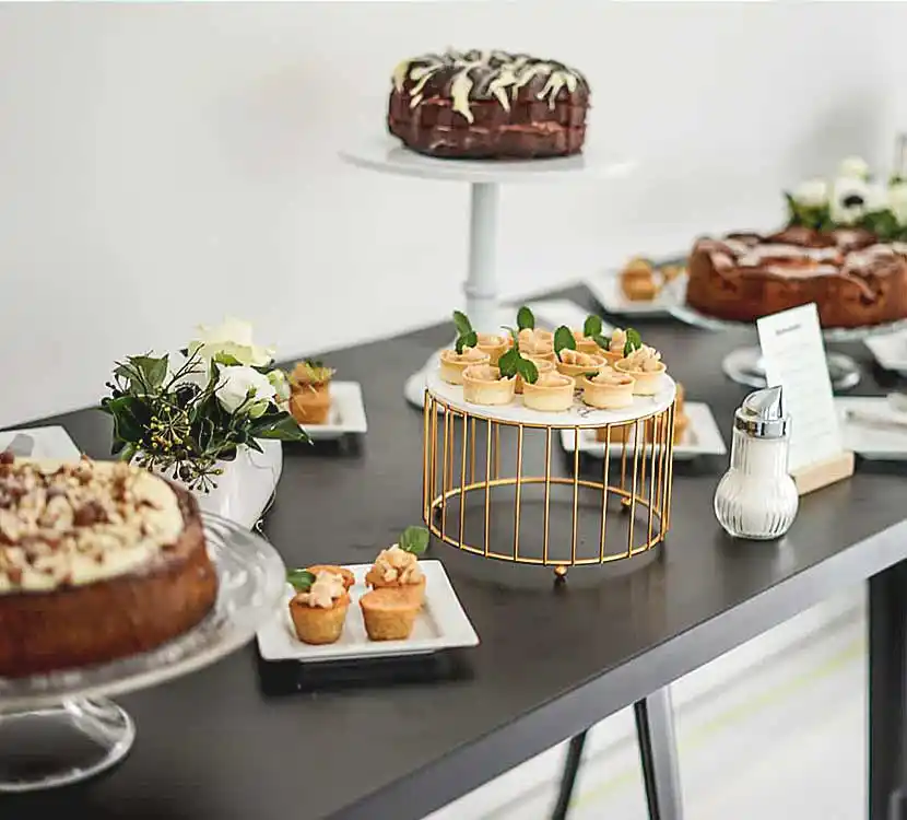 Tisch mit verschiedenen Kuchen und Tartes auf Tellern, Etageren und Platten angerichtet.