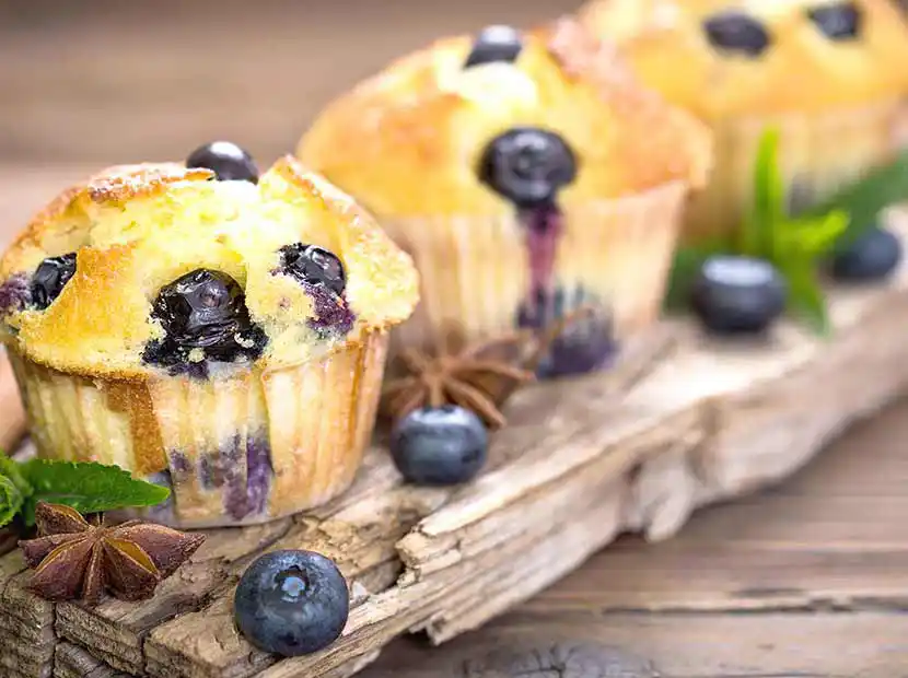 Holzbrett mit drei Blaubeer-Muffins
