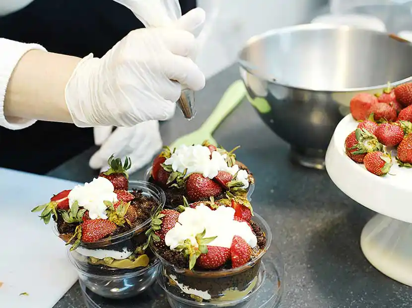 Konditorin sprüht Sahne auf Desserts.