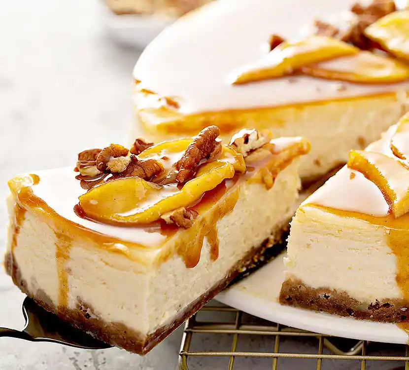 Teller mit angeschnittenem Cheescake mit Karamellsauce, Orangenscheiben und Walnüssen.