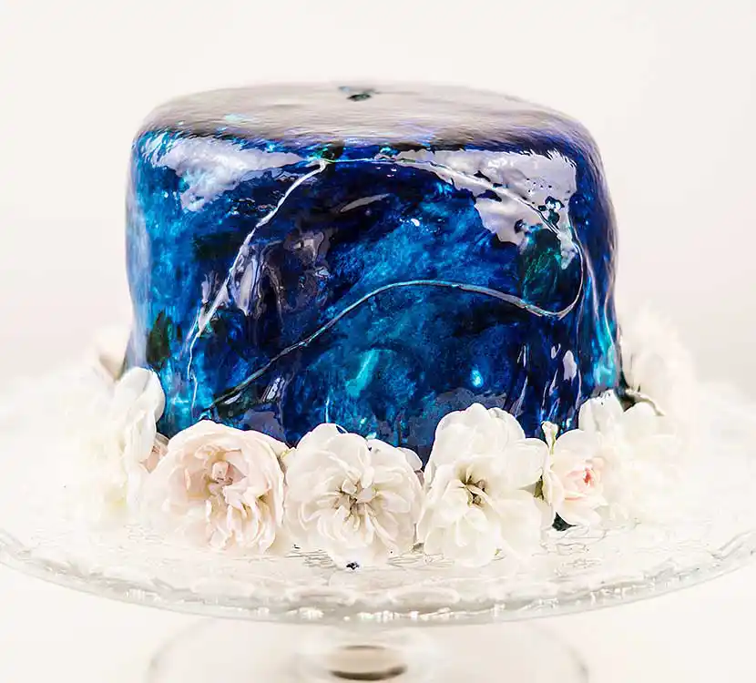 Teller mit blauer, glänzender Torte und Blumendeko.