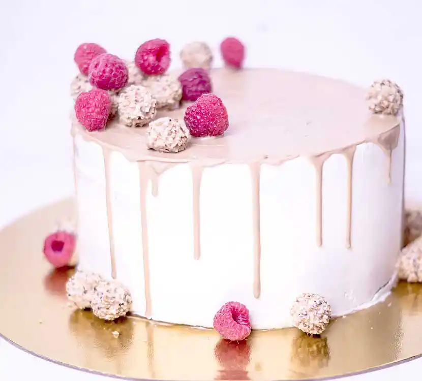 Teller mit weißer Torte und rosa Schoko-Drip und Himbeeren.