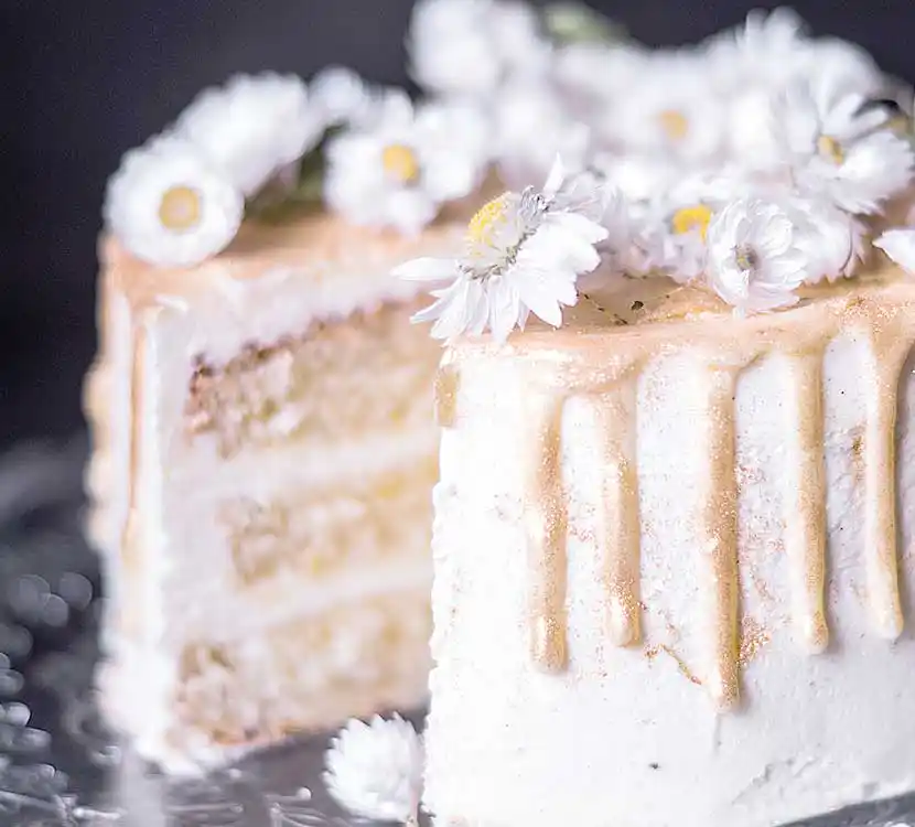 Teller mit angeschnittener weißer Torte mit Mageriten Blumendekor.