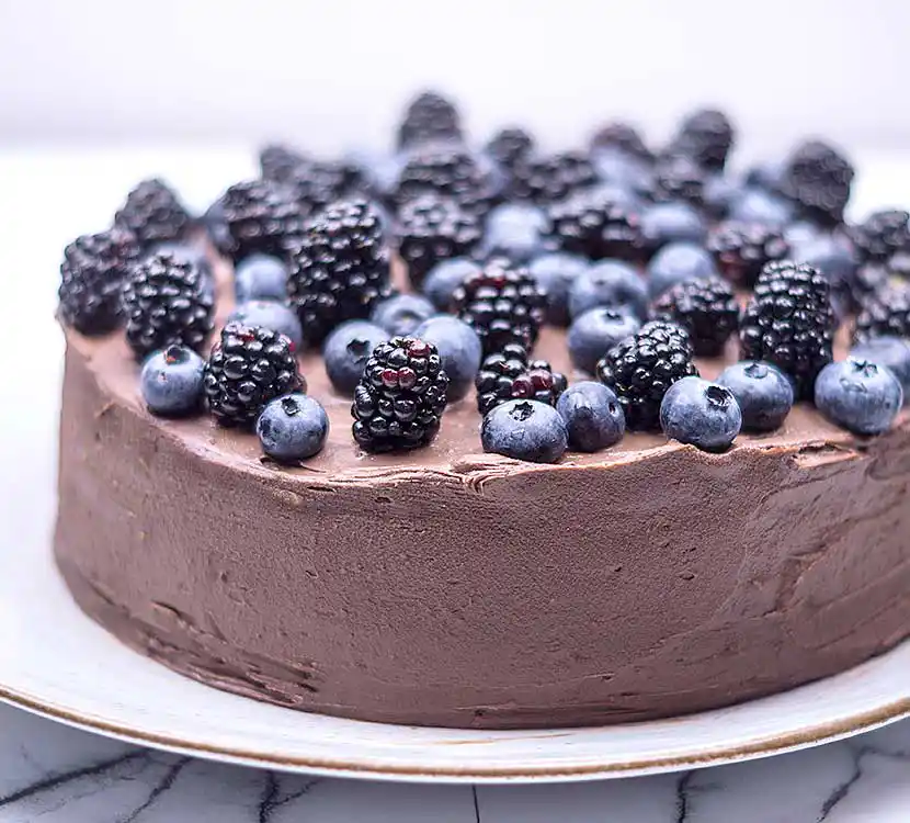 Mit Schoko-Buttercreme eingestrichene Torte und Blau- und Brombeerendeko.