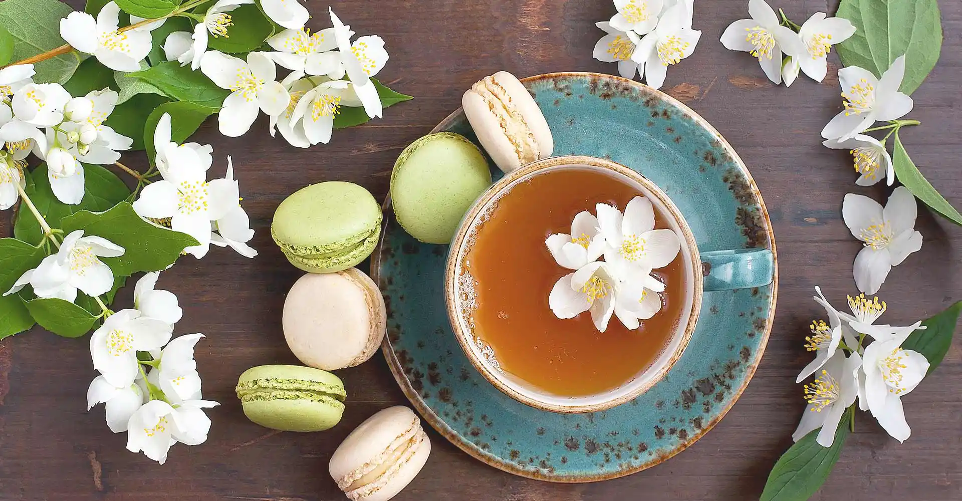 Holztisch mit Lindenblüten, Teetasse und grünen Macarons.