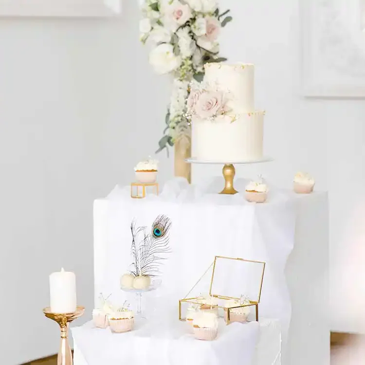 Weißer, gedeckter Tisch mit Hochzeitstorte, Cupcakes und Cakepops auf Teller mit Blumendeko.