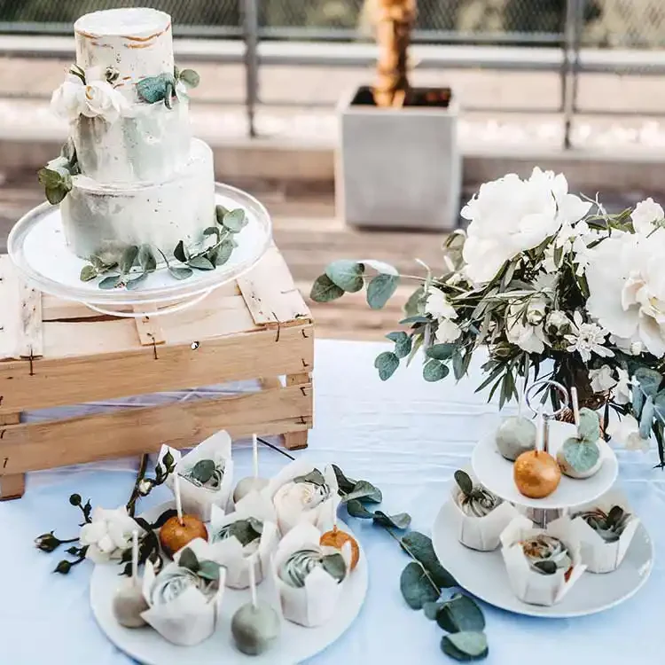 Gedeckter Tisch mit Hochzeitstorte auf Holzkiste, Cupcakes und Cakepops auf Teller.