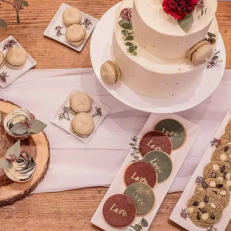 Holztisch mit Hochzeitstorte, Cupcakes und Cookies auf Teller.